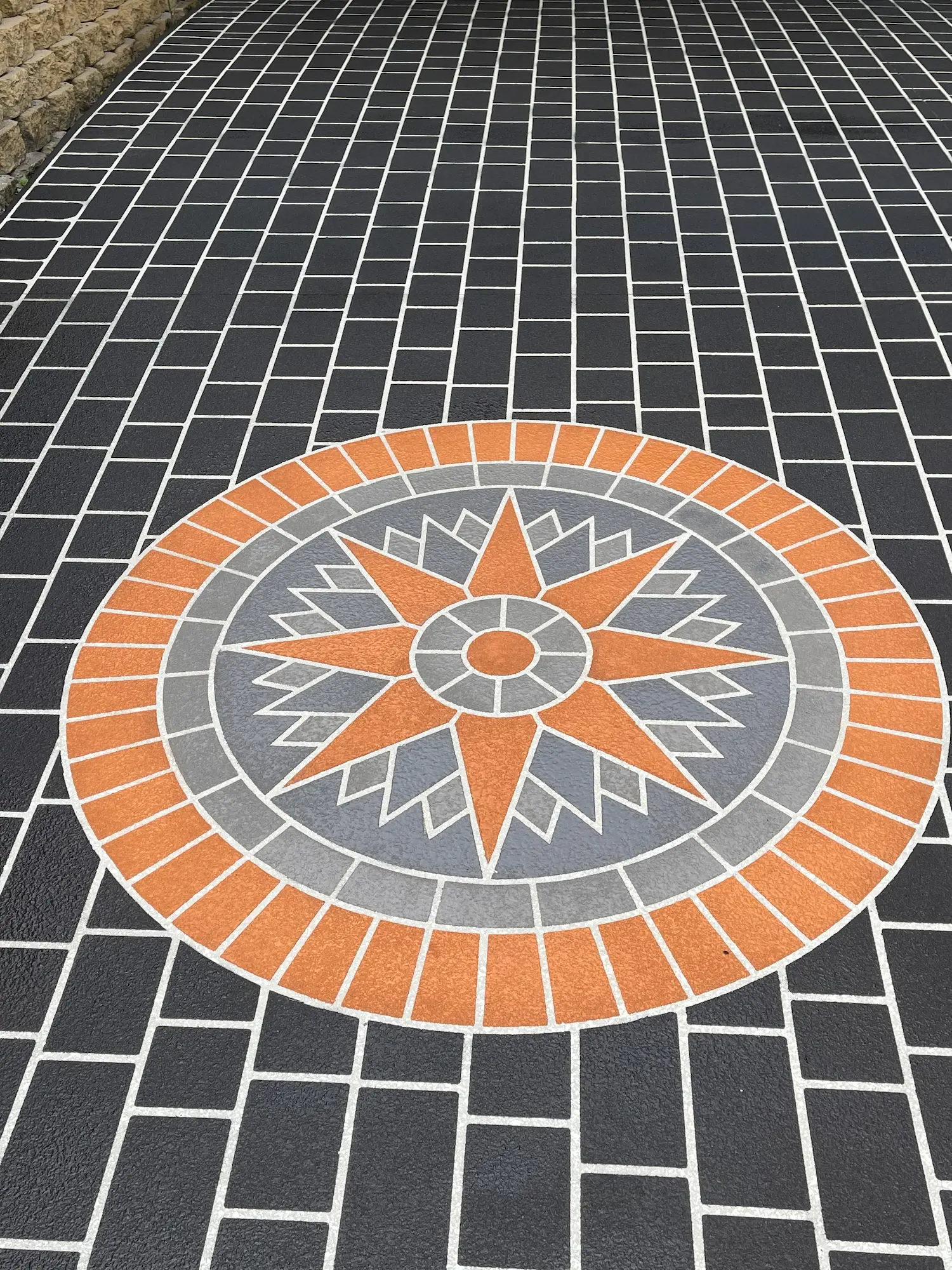 Terracotta star compass feature inlaid in a charcoal brick-pattern spray-crete area